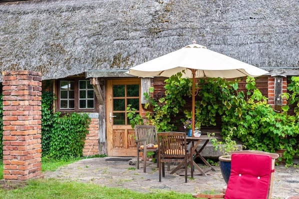 Un bâtiment rustique en bois, doté d’un toit de chaume, d’une cheminée en briques et d’une porte en bois.