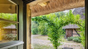 A rustic wooden door opening to a courtyard with a thatched roof, a stone wall, and a small wooden structure. - Holiday Home 'Im Grünen' in the Leonorenwald, Near the Baltic Sea (Borkenhagen / Kalkhorst)