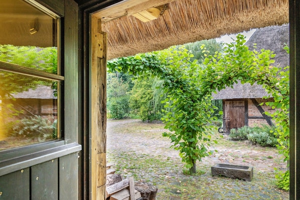 Una puerta de madera rústica que da a un patio con techo de paja, un muro de piedra y una pequeña construcción de madera.