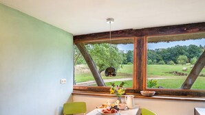 A dining area with a table set for breakfast, a window with a view of a rural landscape, and a hanging light fixture. - Holiday Home 'Im Grünen' in the Leonorenwald, Near the Baltic Sea (Borkenhagen / Kalkhorst)