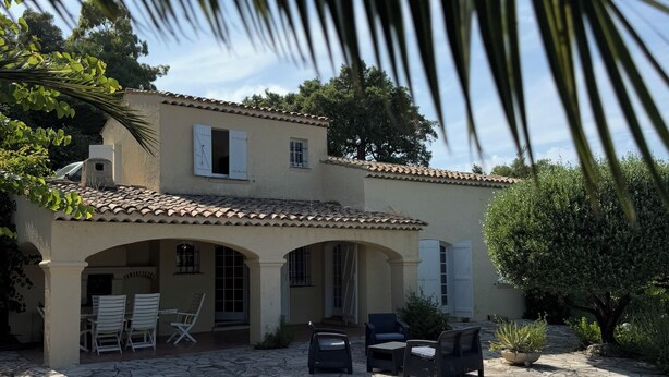 A Mediterranean-style villa with a tiled patio, outdoor seating, and a garden.