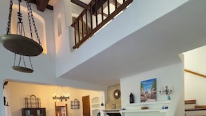 A spacious living room with a large floral sofa, a wooden coffee table, and a fireplace. A staircase with wooden railings leads to an upper level.