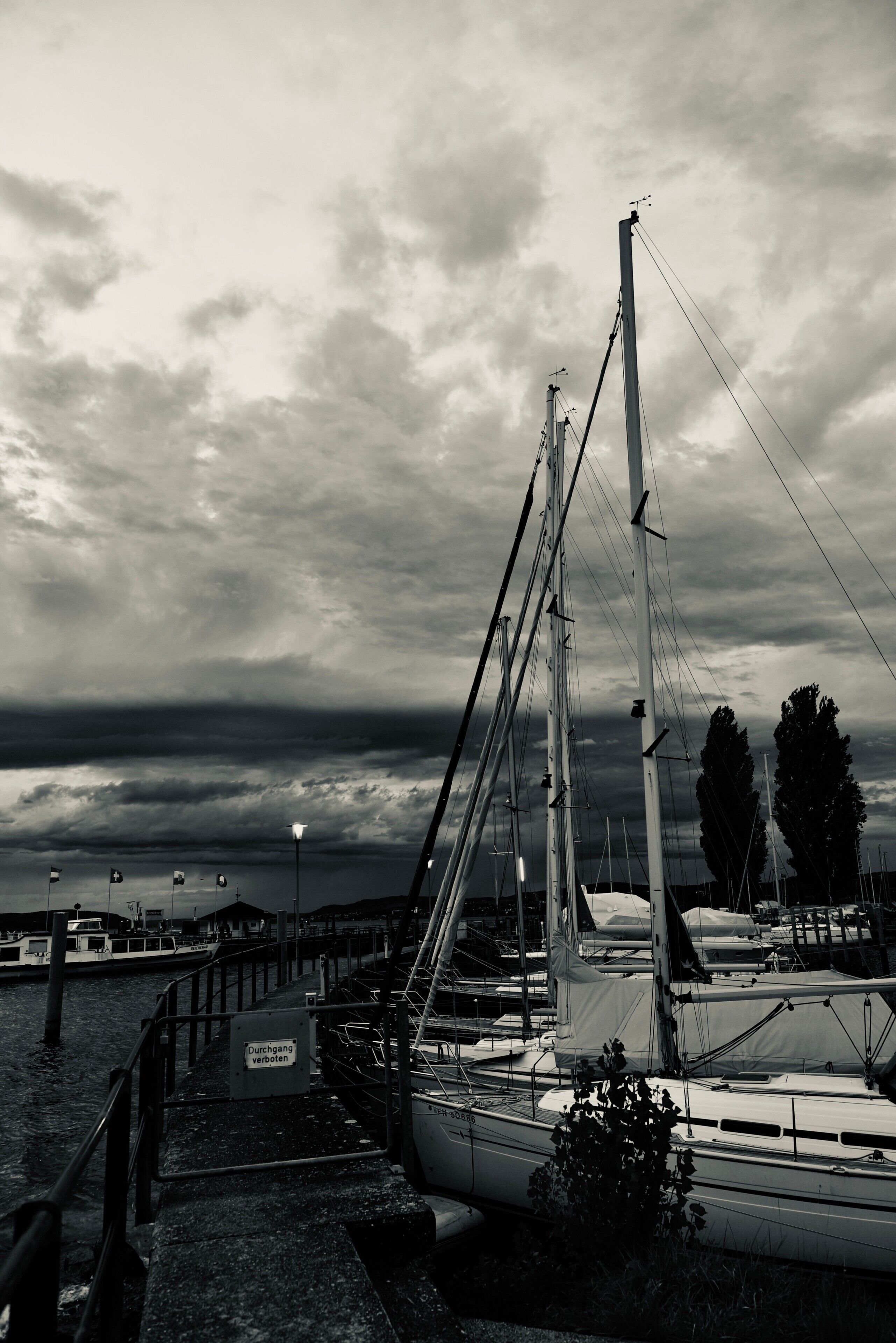 Un port de plaisance avec des bateaux amarrés, un panneau indiquant une zone de baignade et un ciel nuageux.