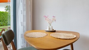A wooden table with two woven placemats, a vase with pink flowers, and a chair.