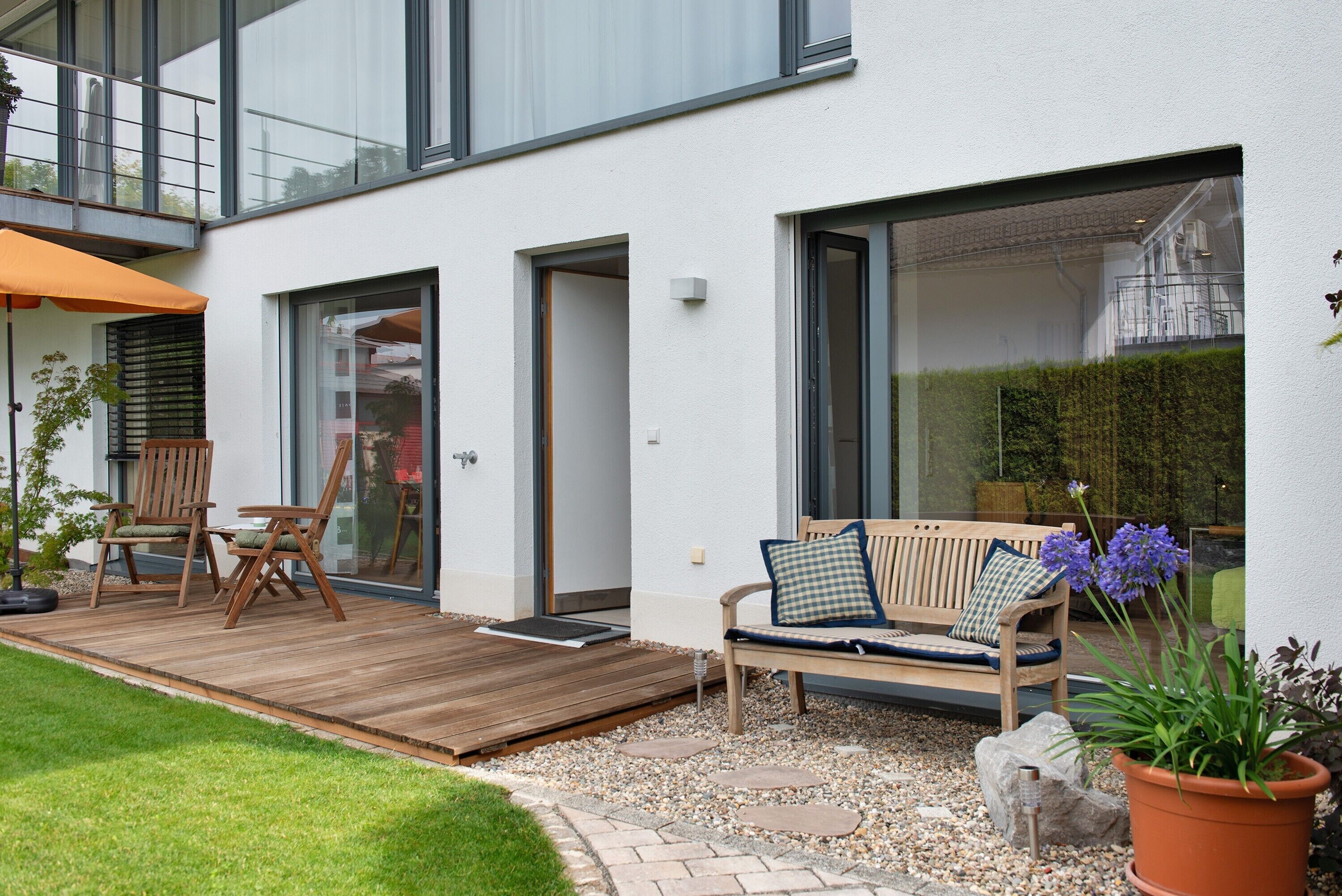 Ein moderner Außenbereich mit Holzdeck, einer Bank mit Kissen und einem Blumentopf.