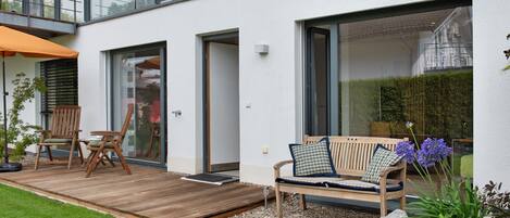 Ein moderner Außenbereich mit Holzdeck, einer Bank mit Kissen und einem Blumentopf.