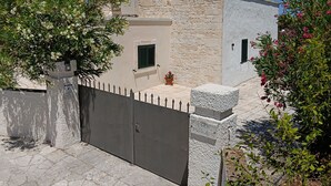 A stone building with a gated entrance, a small window with shutters, and a potted plant on the ledge.