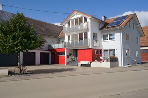 A two-story house with a balcony, a bicycle, and a red garage door.