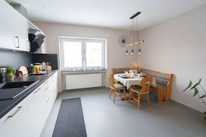 Eine moderne Küche mit Essbereich, ausgestattet mit Backofen, Spüle und einem Fenster mit Jalousien.