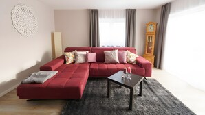 A modern living room with a red sectional sofa, a small table with candles, a decorative wall piece, and a tall wooden clock. - Apartment '1' with Private Terrace, Shared Garden and Wi-Fi (Gammertingen)