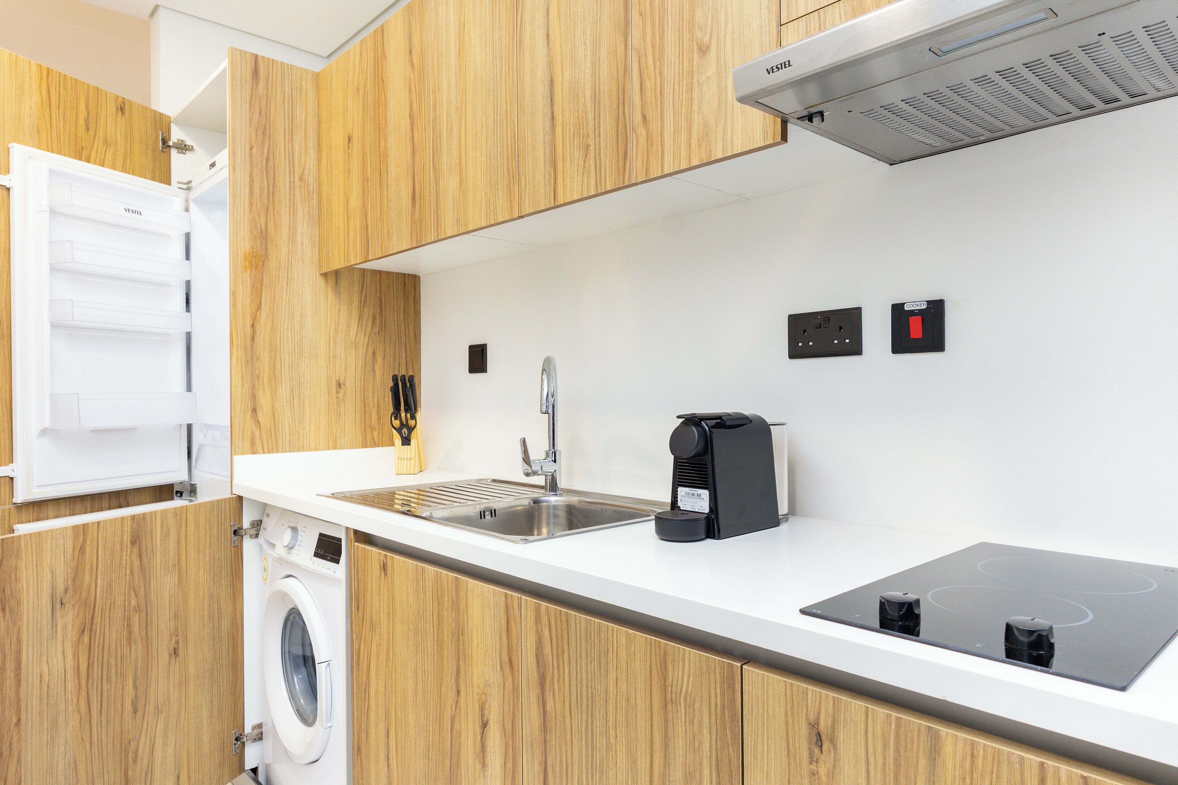 A modern kitchen with wooden cabinets, a built-in washing machine, a sink, and an induction cooktop.