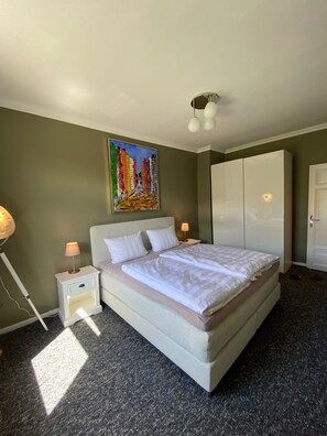 A neatly made bed in a room with a painting on the wall, a wardrobe, and a lamp on the side table. - Apartment '4' with Shared Terrace, Shared Garden and Wi-Fi (Kiel)