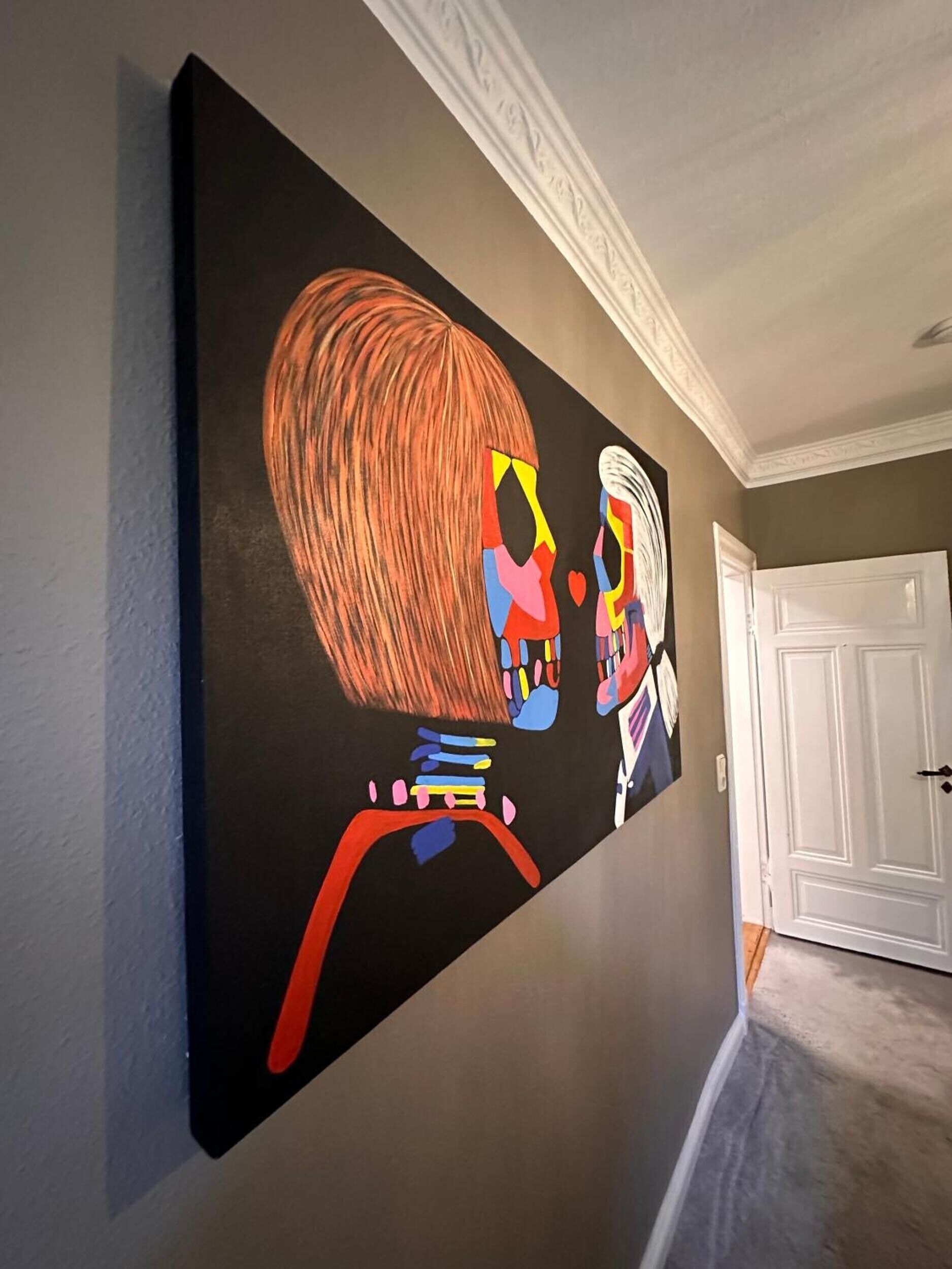 Een hal met een groot abstract schilderij aan de muur, een witte deur en een vloerbedekking.