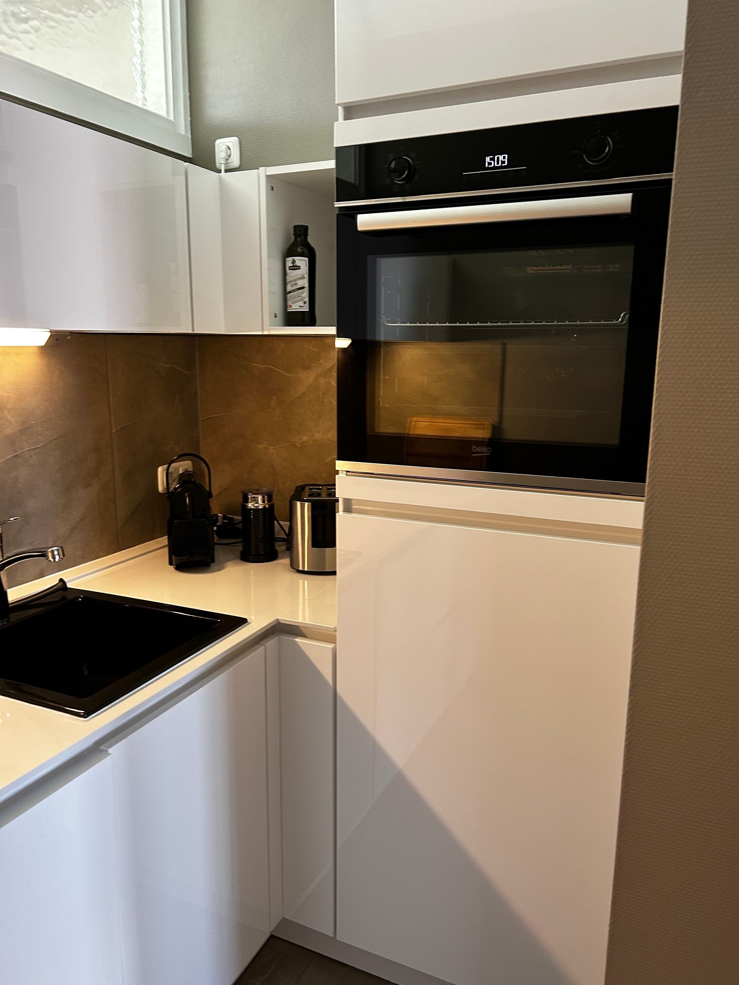 A compact kitchen with a built-in oven, a coffee maker, and a kettle.
