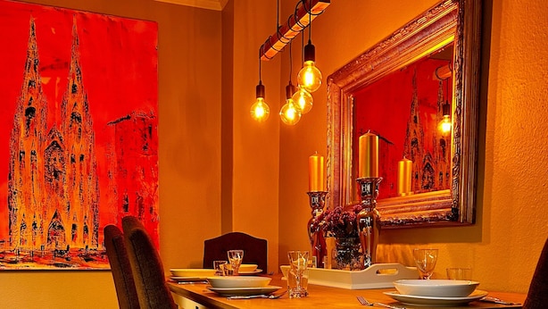 Une salle à manger avec une longue table, des chaises, un lustre et un grand tableau accroché au mur.