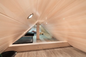 Habitación con techo inclinado, una cama, suelo de madera y vistas a una escalera.