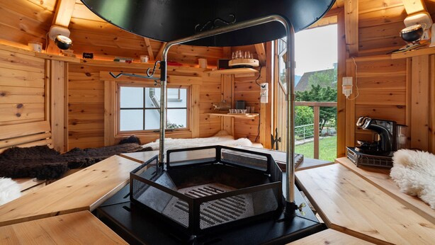 L’intérieur d’un chalet en bois, avec un gril noir au centre, des murs en bois, une fenêtre et un tapis blanc et moelleux.