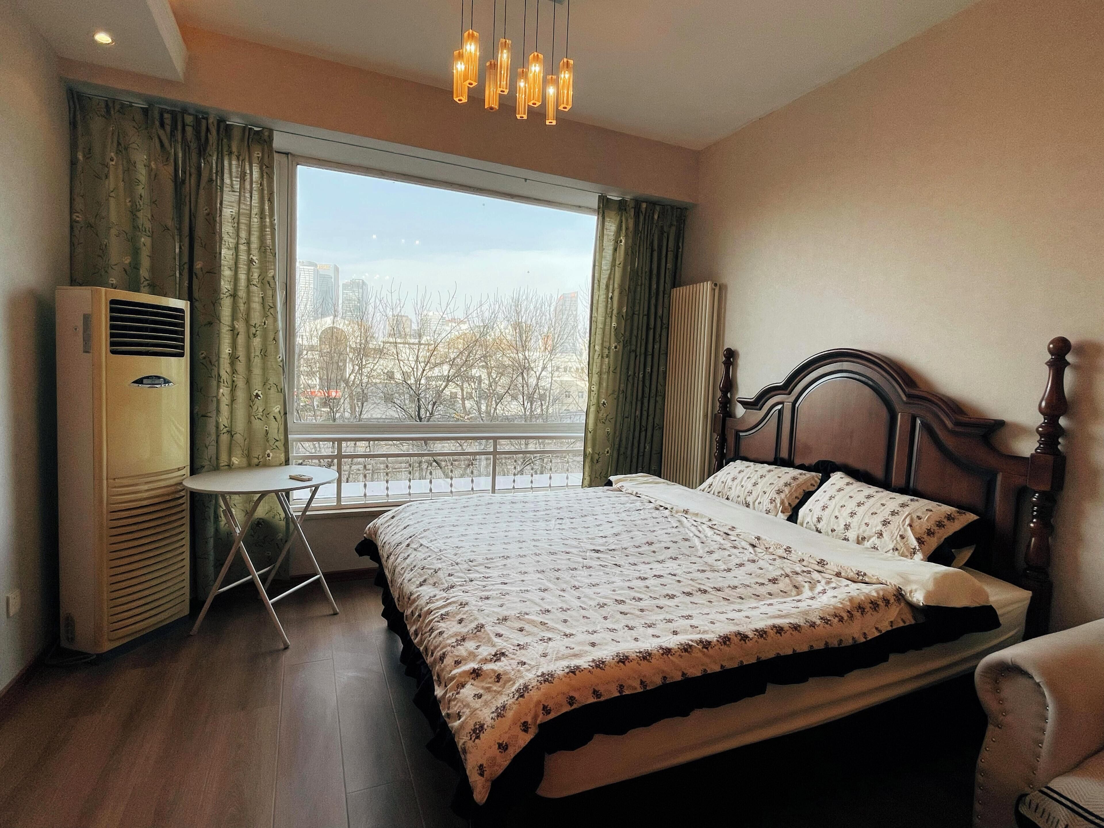 A bedroom with a large bed, a small table, a chair, and a radiator.