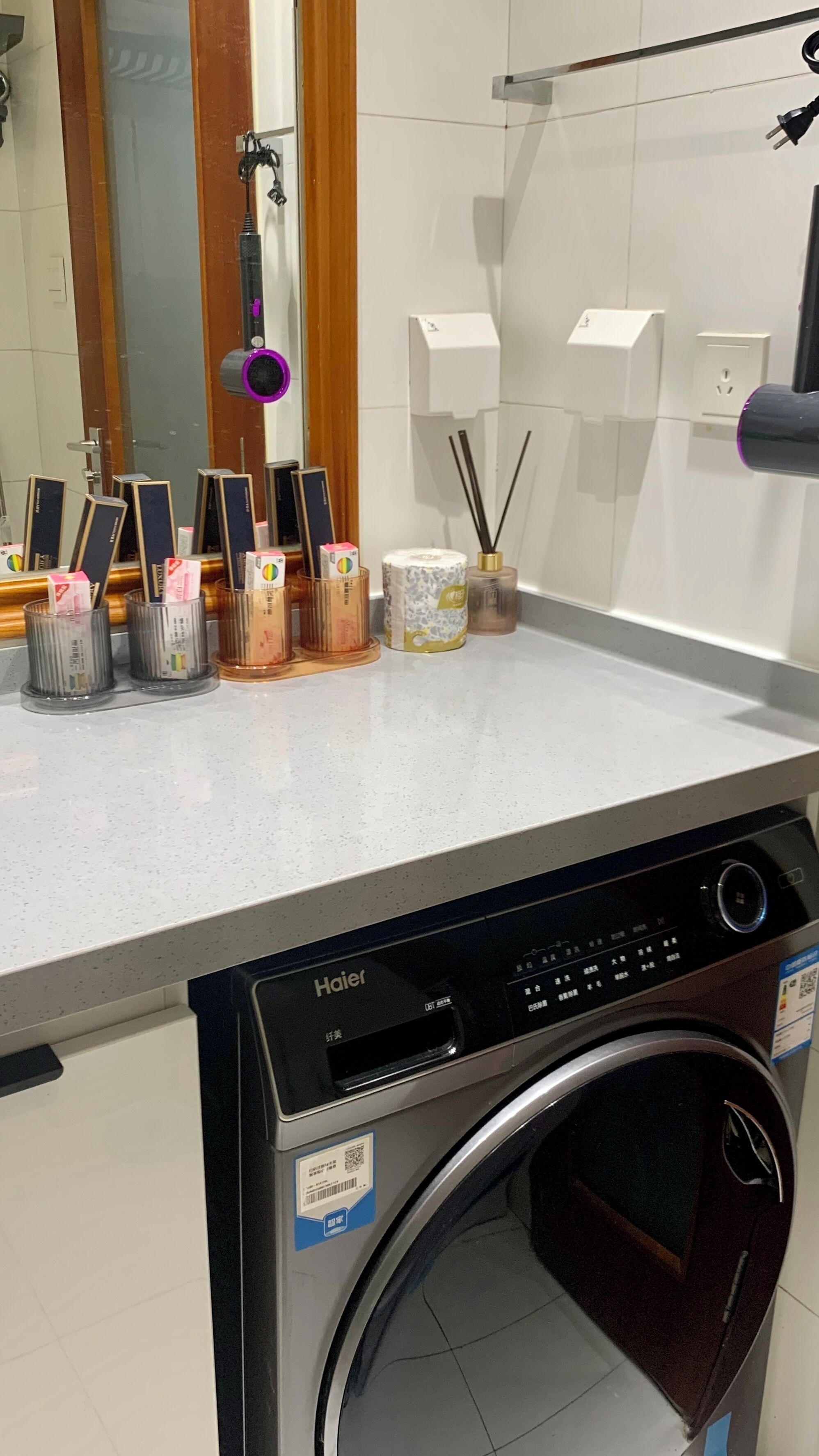 Un espace buanderie équipé d’un lave-linge Haier, d’un miroir et de divers produits de toilette disposés sur le comptoir.