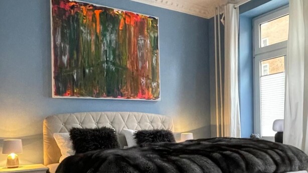 A bedroom with a large bed, a nightstand, a wall painting, and a window with curtains. - Apartment '1' with Shared Terrace, Shared Garden and Wi-Fi (Kiel)