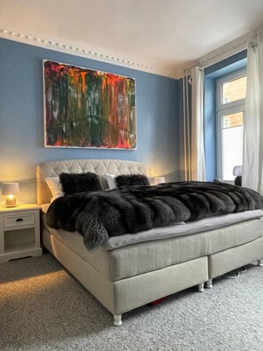 A bedroom with a large bed, a nightstand, a wall painting, and a window with curtains. - Apartment '1' with Shared Terrace, Shared Garden and Wi-Fi (Kiel)