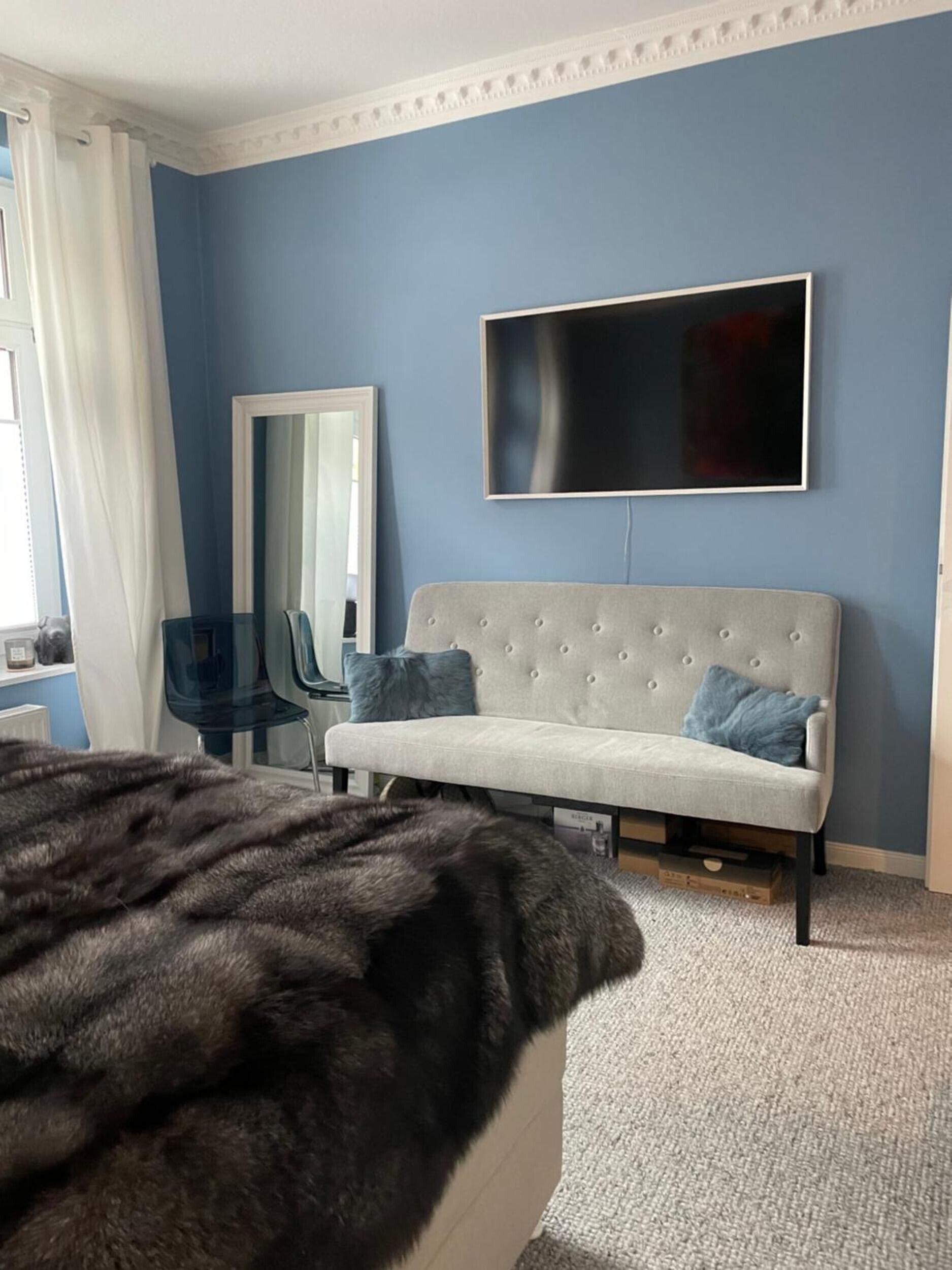 Une chambre à coucher avec un lit, un canapé, une télévision, un miroir et une fenêtre avec des rideaux.