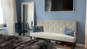 Une chambre à coucher avec un lit, un canapé, une télévision, un miroir et une fenêtre avec des rideaux.