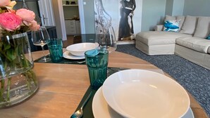 Un comedor con una mesa lista para dos personas, un jarrón de flores y un cuadro en la pared.