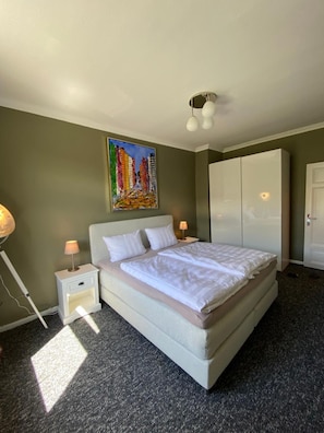 A bedroom with a bed, a nightstand, a lamp, a wardrobe, and a painting on the wall.