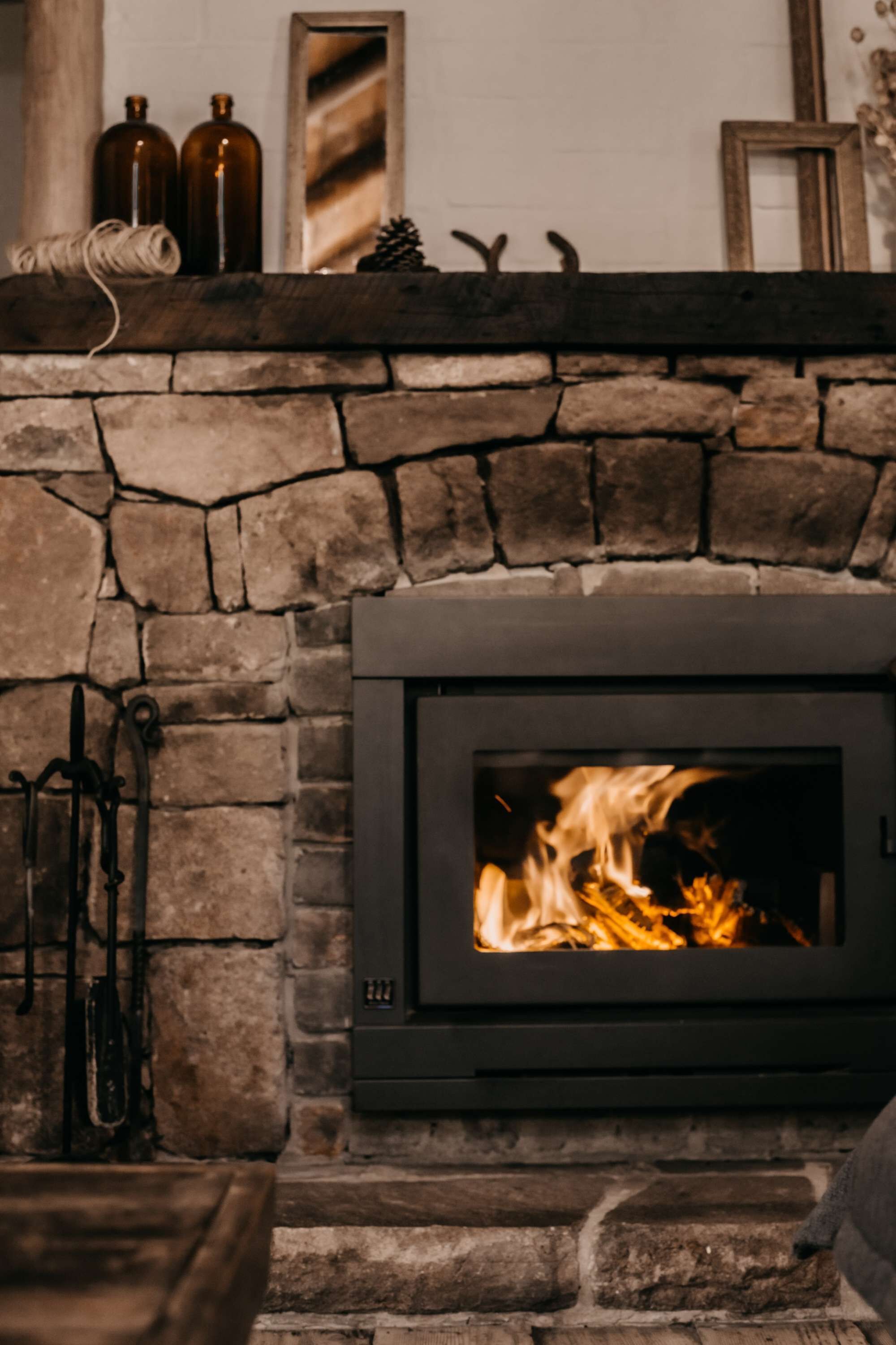 Una chimenea de piedra con un estufa de leña moderna, un repisa de madera con adornos, y una pared de piedra rústica.