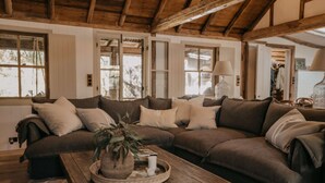 Una sala de estar acogedora con un amplio sofá modular, una mesa de centro de madera con una planta y ventanas grandes que dejan entrar luz natural.