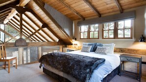 Een slaapkamer met een groot bed, houten balken, een raam met ruitverdeling en een klein tafeltje met een lamp.