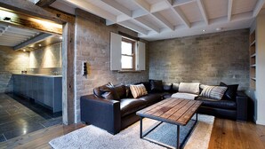 Een moderne woonkamer met een leren bank, een houten salontafel en een keuken die door een open deur zichtbaar is.