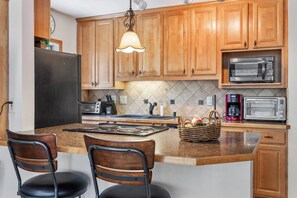 A kitchen with wooden cabinets, a stove, a microwave, a toaster, and a hanging light fixture. - Cozy Mountain Get away (Copper Mountain)