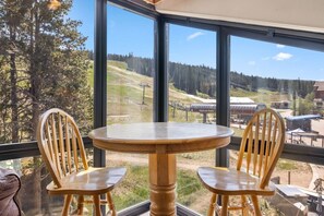 A room with a large window offering a view of a ski resort and a chair with a wooden table. - Cozy Mountain Get away (Copper Mountain)