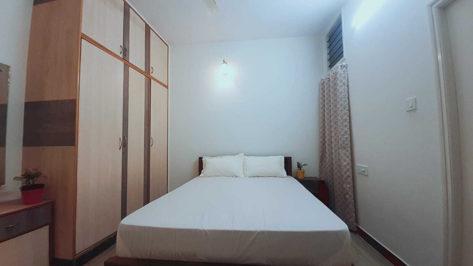 A bedroom with a bed, a wardrobe, a nightstand, and a potted plant.