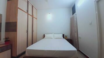 A bedroom with a bed, a wardrobe, a nightstand, and a potted plant.