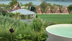 A view of a lakeside property with a thatched-roof building, a large water tank, and a lush green landscape.