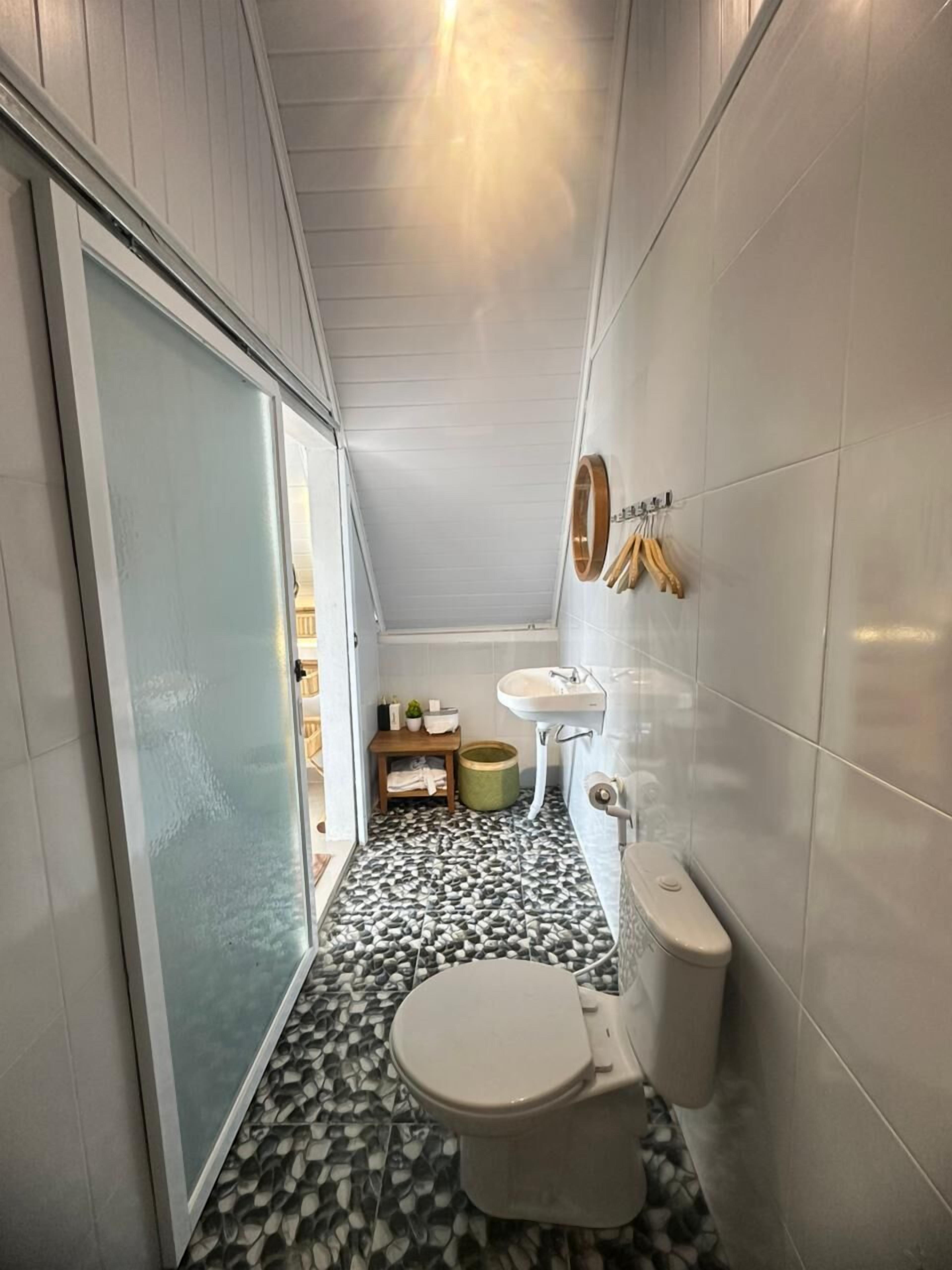 A narrow bathroom with a toilet, sink, and a small shelf with toiletries.