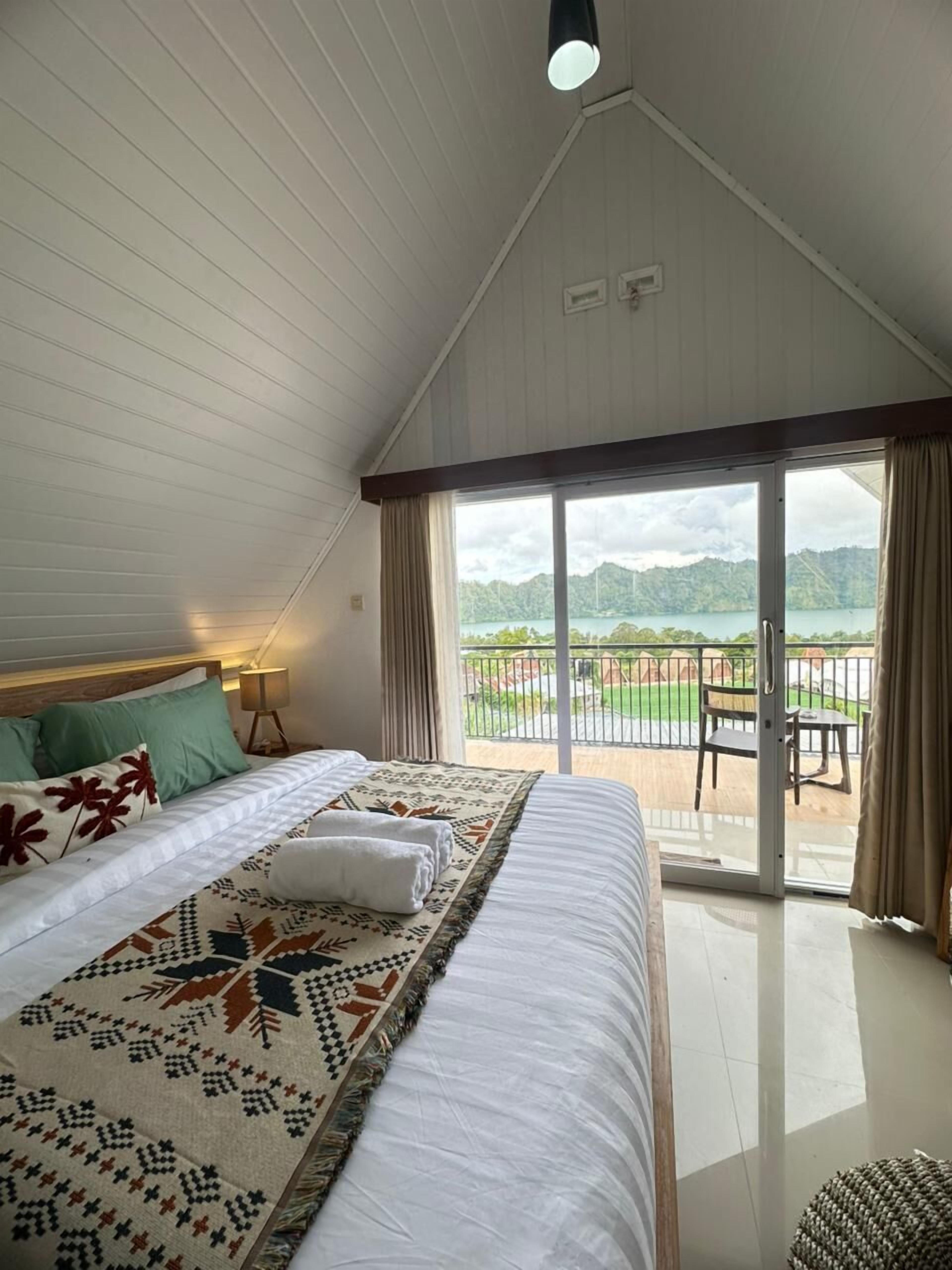 A bedroom with a large bed, a view of a deck, and a balcony.