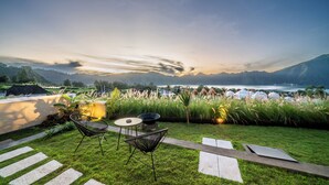 A patio with a view of a lake and mountains, featuring a table and chairs, and a fire pit.