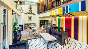 A vibrant hostel interior with a colorful striped wall, a reception desk, and a seating area with tables and chairs. - Lamoon Vivit (Bangkok)