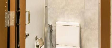 A compact bathroom with a toilet, a small trash bin, and a shower area.