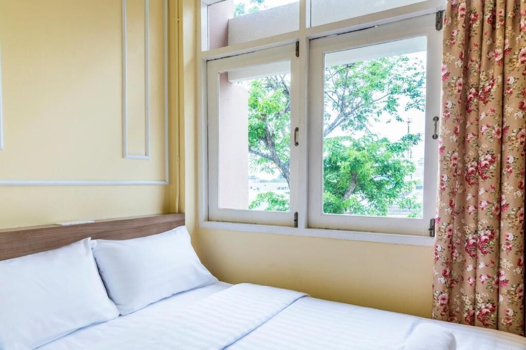 A hotel room with a bed, two windows, and a view of trees outside.
