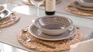 Une table à manger dressée avec un set de table en fibres tressées, un bol, une assiette, une fourchette et une bouteille de vin.
