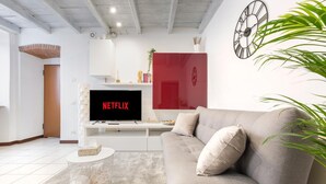 Un salon moderne avec un canapé gris, un meuble de rangement blanc et un téléviseur affichant le logo « NETFLIX ».
