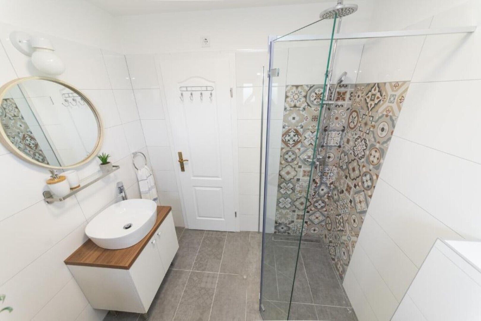 Une salle de bain avec un lavabo blanc, un miroir et un espace douche agrémenté de carreaux à motifs.