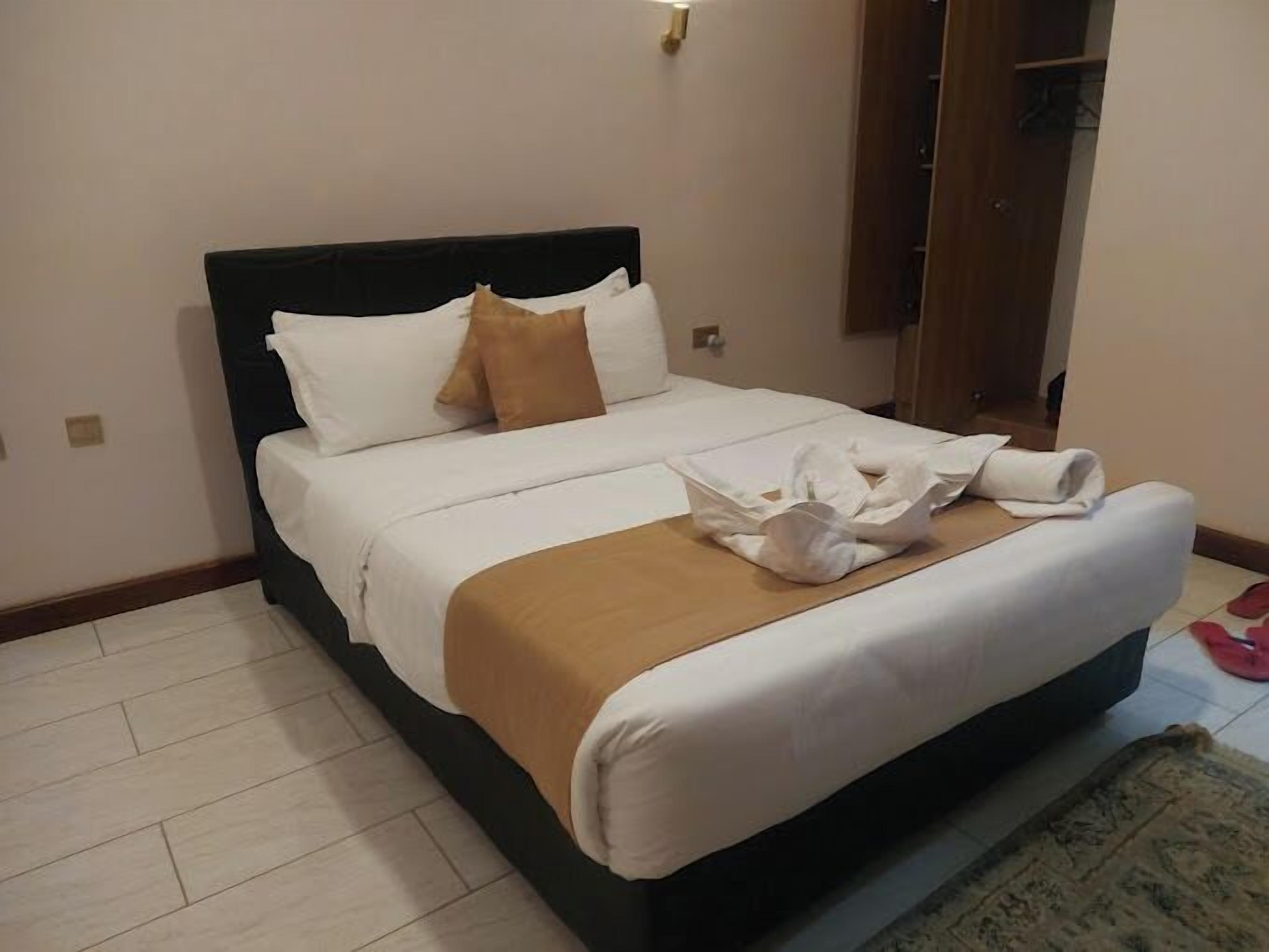 A neatly made bed with white and brown linens, a wooden headboard, and a small bedside table with a lamp.