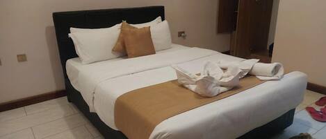 A neatly made bed with white and brown linens, a wooden headboard, and a small bedside table with a lamp.