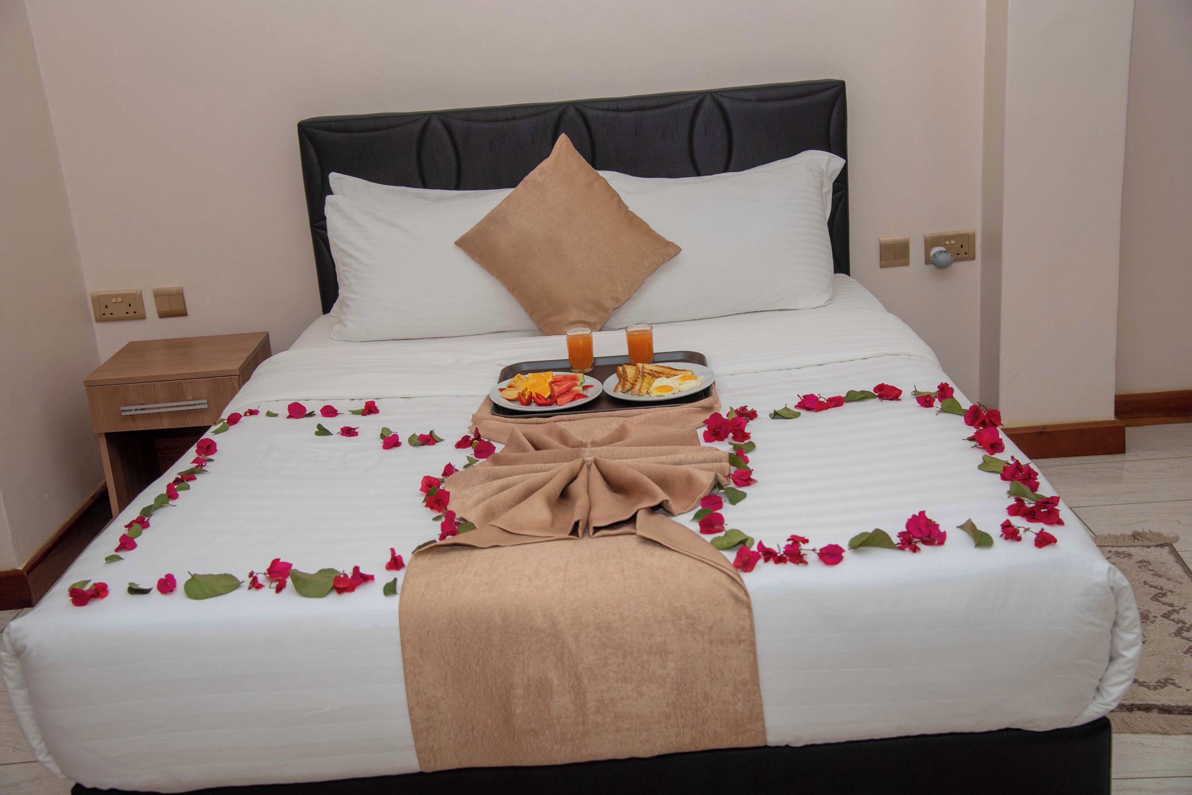 Uma cama bem arrumada com bandeja de café da manhã, almofadas e flores decorativas.